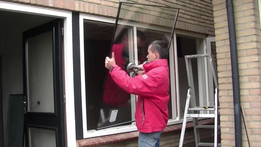Vitrier professionnel retirant un vieux simple vitrage pour installer un double vitrage HR++ sur un châssis en bois conservé à Anderlecht.